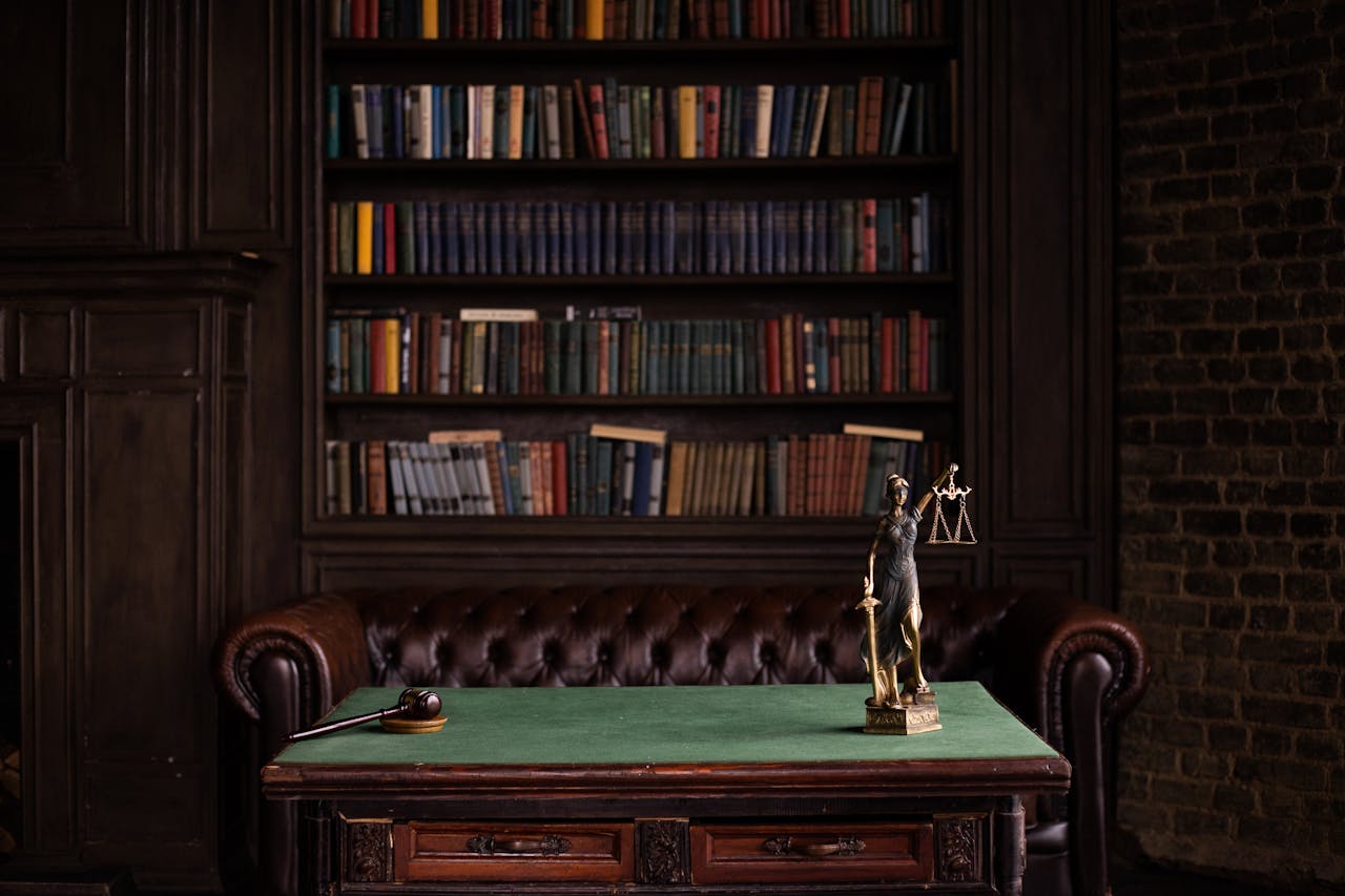 service-01 A classic study room with shelves of books, a gavel, and Lady Justice figurine on a green table.