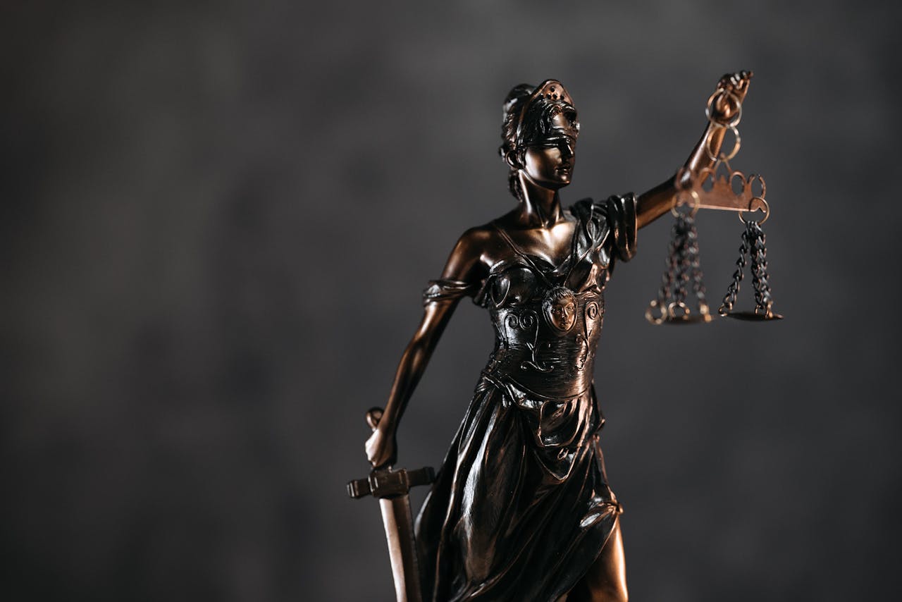 services-img Detailed bronze Lady Justice statue with scales and sword against a dark background, symbolizing law and justice.